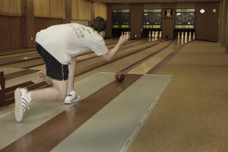 Junger Mann in Sportkleidung wirft eine Bowlingkugel auf einer Bahn in einer Kegelhalle.